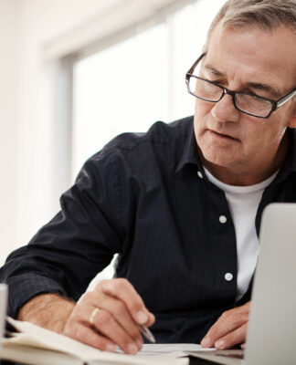 Man on laptop at desk checking papers